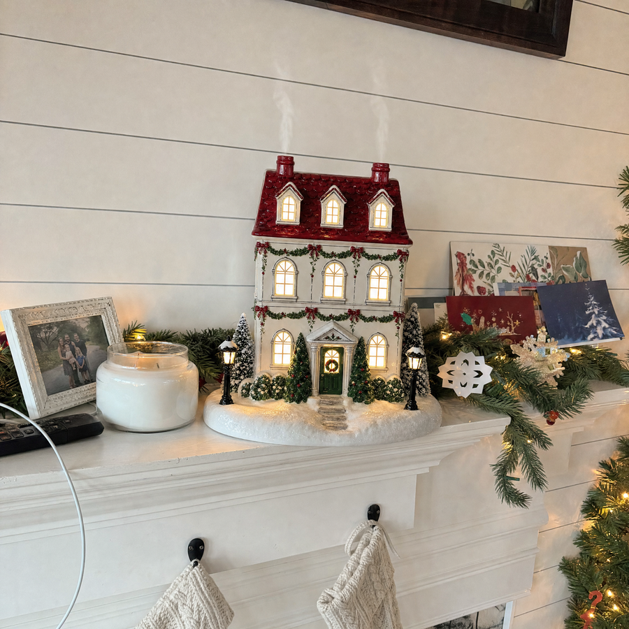 Christmas house diffuser with glowing windows on a decorated mantel
